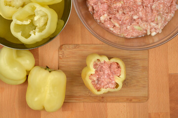 A top-down view shows a raw pepper being stuffed with a mixture of ground meat, rice, and onions, with other cleaned peppers and the meat mixture bowl nearby