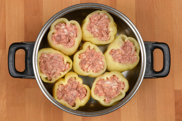 A top-down view shows seven raw bell peppers, generously filled with a mixture of ground meat, rice, and onions, neatly arranged within a cooking pot, ready for preparation