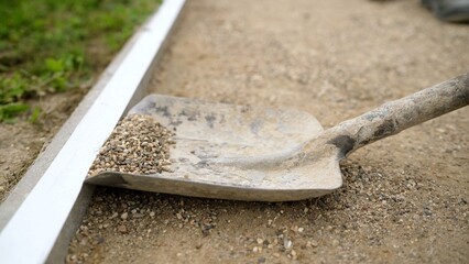 Construction worker spreading gravel with shovel along concrete border