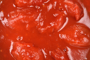 A close-up, top-down view captures whole peeled tomatoes immersed in a thick, vibrant red tomato...