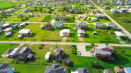 Vibrant stilted beach houses with rooftop decks line a coastal neighborhood in Port Bolivar, Texas. RVs parked nearby on concrete pads and grass highlight modular living and Gulf Coast vacation