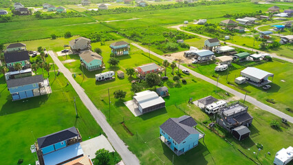 Vibrant stilted beach houses with rooftop decks line a coastal neighborhood in Port Bolivar, Texas. RVs parked nearby on concrete pads and grass highlight modular living and Gulf Coast vacation