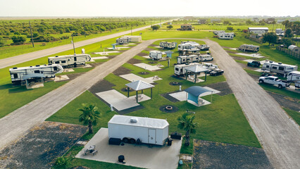 Coastal RV Park along Texas State Highway 87 in Port Bolivar. Neat rows of RVs on concrete pads with picnic setups. Gravel roads weave through green landscape near beachfront residential zones