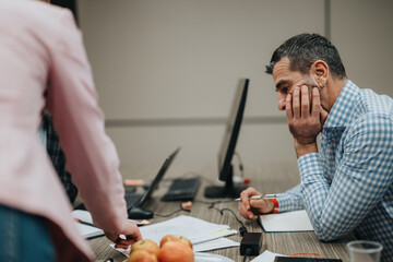 A thoughtful professional brainstorming solutions while reviewing documents with a colleague during...