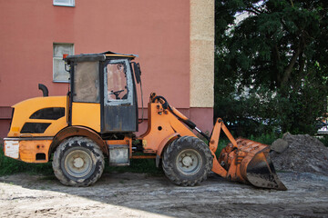 Powerful construction vehicle rests near a building surrounded by trees in a serene urban setting