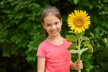 Smiling White girl holding bright sunflower in summer garden. Concept of childhood joy, nature, and innocence