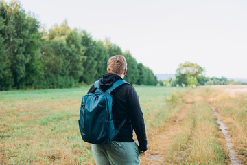 Rear view of blonde man with backpack standing in the countryside. Traveler. Summer time. Portrait...