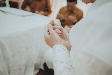Close-up of Muslim bride praying during Islamic wedding ceremony in Indonesia, hands in dua position wearing lace white dress, spiritual moment of devotion and tradition