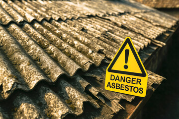 WARNING SIGN WITH EXCLAMATION MARK AND TEXT "DANGER ASBESTOS" ON CORRUGATED ASBESTOS CEMENT ROOF, symbolizing health risk and hazardous material exposure