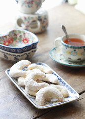 Traditional german cookies Vanillekipferl in the shape of half moons, sprinkled with powdered sugar. Beautiful ceramic cup and saucer in the background. Selective focus.