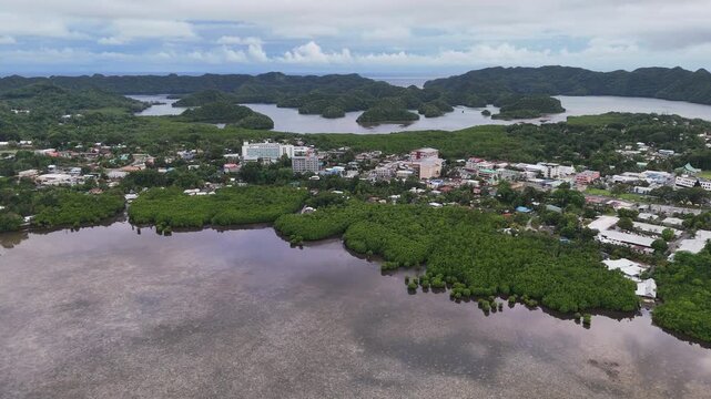 Dynamic drone shot gliding around the small island town and green-covered terrain in Palau. Wide cinematic drone shot.