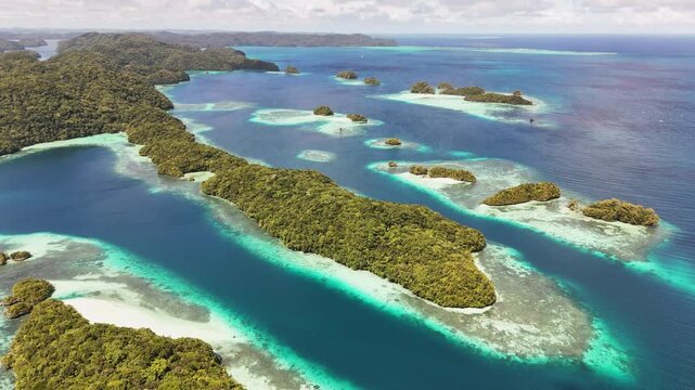 Dynamic drone shot revealing and showcasing the crystal blue waters and rocky, forested islands around Palau.