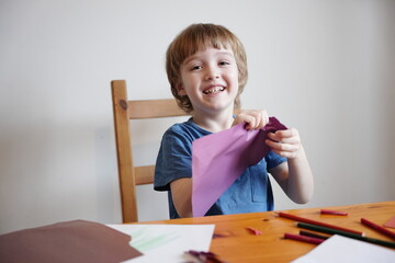 A five year old boy with blond hair plays and engages himself with colored paper. He is fooling...