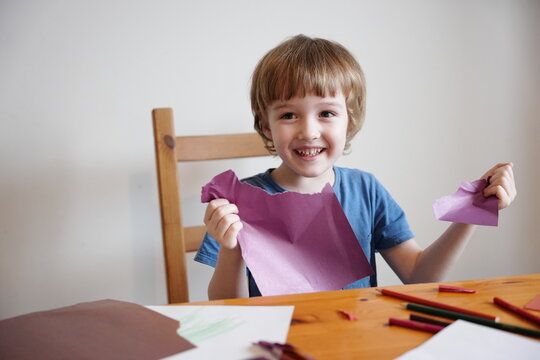 A five year old boy with blond hair plays and engages himself with colored paper. He is fooling around, having fun and tearing paper.