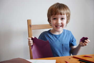 A five year old boy with blond hair plays and engages himself with colored paper. He is fooling...
