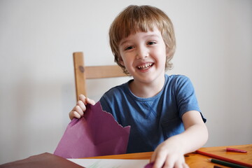 A five year old boy with blond hair plays and engages himself with colored paper. He is fooling...