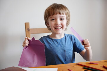 A five year old boy with blond hair plays and engages himself with colored paper. He is fooling...