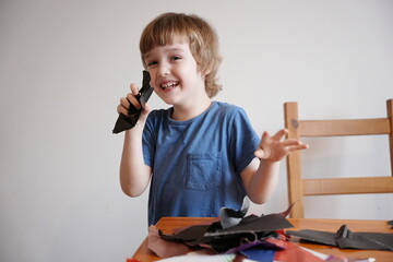A five year old boy with blond hair plays and engages himself with colored paper. He is fooling...