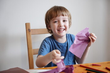 A five year old boy with blond hair plays and engages himself with colored paper. He is fooling...