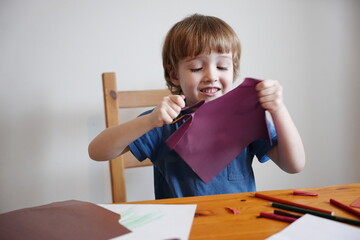 A five year old boy with blond hair plays and engages himself with colored paper. He is fooling...