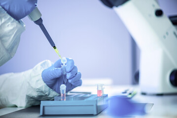 Scientist in laboratory using pipette and microscope for research