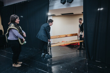 A team of enthusiastic young actors collaborates on stage during a theater rehearsal, arranging...
