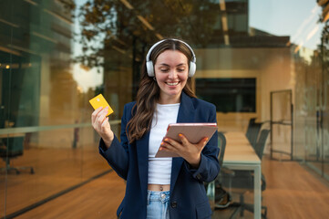 Businesswoman using tablet and credit card for online shopping while listening to music with headphones