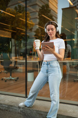 Young woman enjoying coffee and tablet outside modern office building