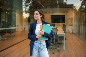 Young businesswoman holding folders is waiting in front of the office building