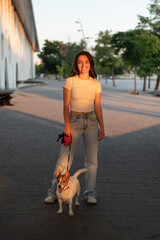Young woman walking with her jack russell terrier at sunset in the city