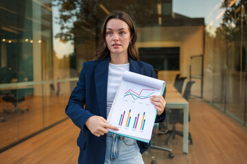 Businesswoman showing charts and statistics on paper in front of office building