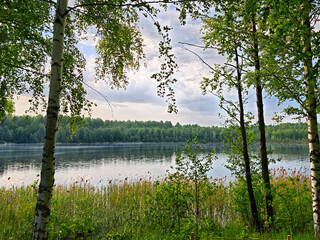 Obraz premium The tranquil lakeside scene features vibrant greenery surrounding the clear water, which beautifully mirrors the sky above.