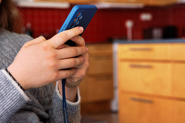 Closeup of hands using smartphone in home kitchen setting in the blurred background. Selective...