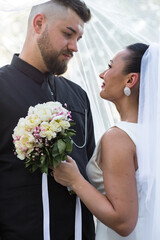 Bride and groom look deeply into each other’s eyes, holding a bouquet. Tender moment captured in...
