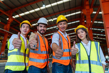 Team engineer working hard in factory. They are showing thumbs up and looking at the camera.