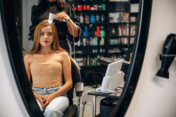 Customer is sitting on the chair. Woman is in a beauty salon with hair stylist