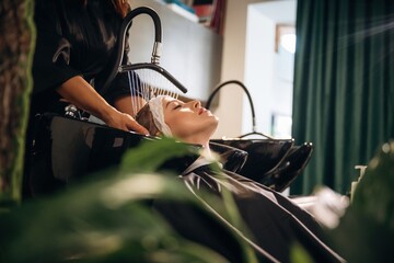 Lying down, washing the hair. Woman is in a beauty salon with hair stylist