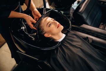 Service for customer, washing head. Woman is in a beauty salon with hair stylist