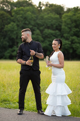 A man opens a bottle of champagne while a woman in a white dress smiles beside him - a fun and...