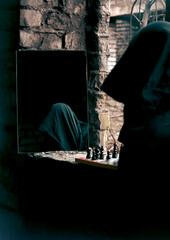 Mysterious Hooded Figure Reflected In Mirror Beside A Chessboard In Abandoned Room, Dim Lighting.