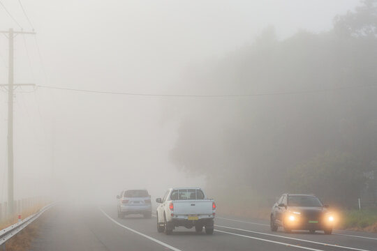 Cars travelling on highway road through fog with low visibility