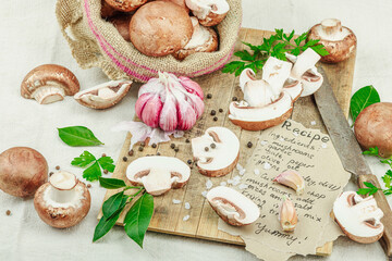 Rustic flat lay with fresh brown mushrooms, garlic, parsley, knife and handwritten recipe