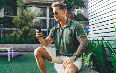 Stylish young man using smartphone confidently, absorbed in digital experience, presenting balance...