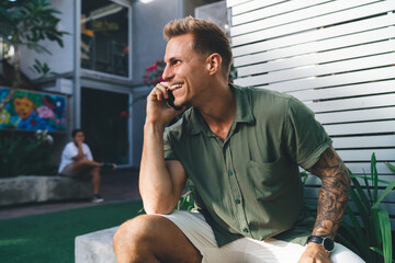 Tattooed man smiling wide on phone, relaxed posture, combining mobile connectivity with natural...