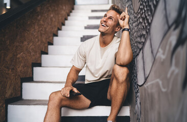 Smiling man pointing upward with smartphone, celebrating fresh tech idea, highlighting joy of...