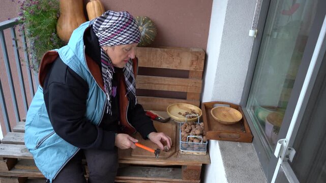 Crack nuts with a hammer. An elderly woman peels a walnut. Grandmother hands cracking nutshell