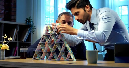 Indian Businessmen building playing cards tower at office desk symbolizing teamwork and business strategy - Powered by Adobe