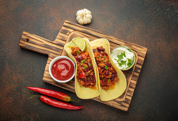 Delicious tacos with chili con carne, lime, ketchup, and sour cream on a wooden board with fresh...
