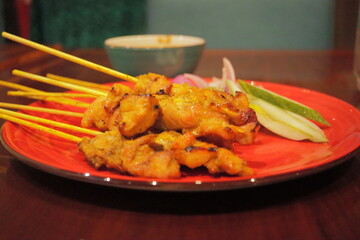 Delicious Grilled Chicken Satay Skewers on Red Plate – Traditional Southeast Asian Street Food with Peanut Sauce, Served with Cucumber and Onion Slices – Close-Up Food Photography