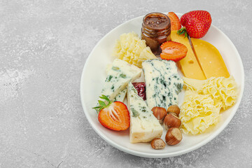 Cheese assortment on wooden boards with strawberries, nuts and jam on stone background